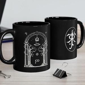 May include: Two black ceramic mugs with white designs. One mug features a white illustration of an archway with trees and a star. The other mug has a white circle with a symbol inside.