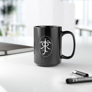 May include: Black ceramic coffee mug with a white circle design featuring a stylized symbol. The symbol is a stylized version of the Japanese character for "East".