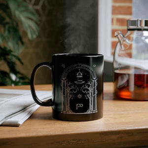 May include: Black ceramic mug with a white design of a doorway with a star and a symbol. The mug has the words "Not all those who wander are lost" written around the top.