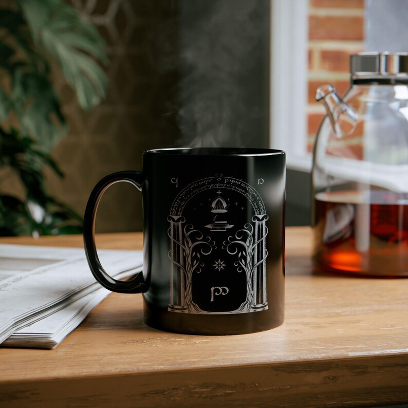 May include: Black ceramic mug with a white design of a doorway with a star and a symbol. The mug has the words "Not all those who wander are lost" written around the top.