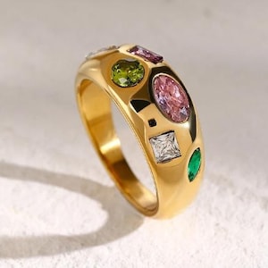 May include: A gold ring with a wide band and colorful gemstones. The ring features a variety of shapes and sizes of green, pink, and clear stones.