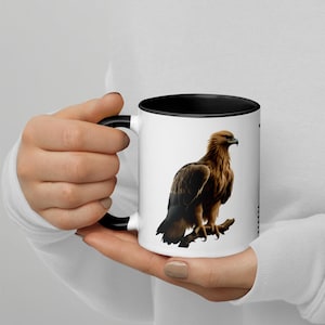 Peut inclure: Mug en céramique blanche avec intérieur et anse noirs. L'illustration détaillée représente un aigle brun perché sur une branche. L'aigle a un bec pointu et regarde vers la droite. La tasse est tenue par une personne.