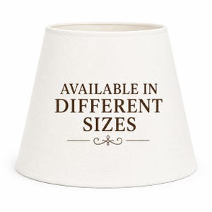 May include: A conical off-white lampshade featuring the dark brown text "AVAILABLE IN DIFFERENT SIZES" centered on the front, accompanied by a decorative flourish line underneath the text. The lampshade has a smooth, solid-colored fabric surface.