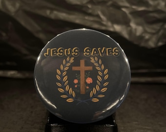 May include: A blue button with the text "JESUS SAVES" in yellow letters. A brown wooden cross with a gold outline is surrounded by a wreath of gold leaves with pink flowers.