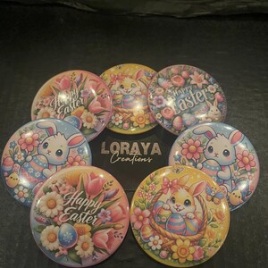 May include: Six colorful round buttons with Easter themes. Each button features a different design with bunnies, eggs, flowers, and the text "Happy Easter".