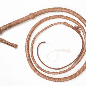 May include: A brown leather bullwhip with a braided design. The whip is coiled and has a handle with a tassel.