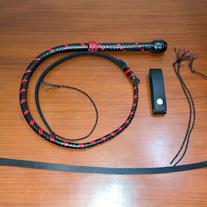 May include: A black leather whip with red stitching. The whip is coiled and has a handle with a black leather strap. There are also three black leather cords with tassels.