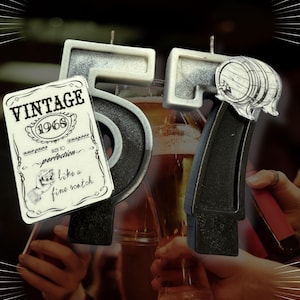 May include: A birthday candle set shaped as the number 57, with a vintage label that reads "Vintage 1968". The candle has a black and silver color scheme, with a small barrel illustration on the number 7. The background includes glasses of beer.
