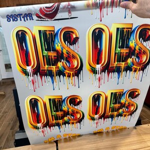 May include: A white background with the words "I AM A STAR" printed in black and the word "OES" printed in large, colorful, dripping letters. The letters are gold with rainbow-colored paint dripping down the sides.