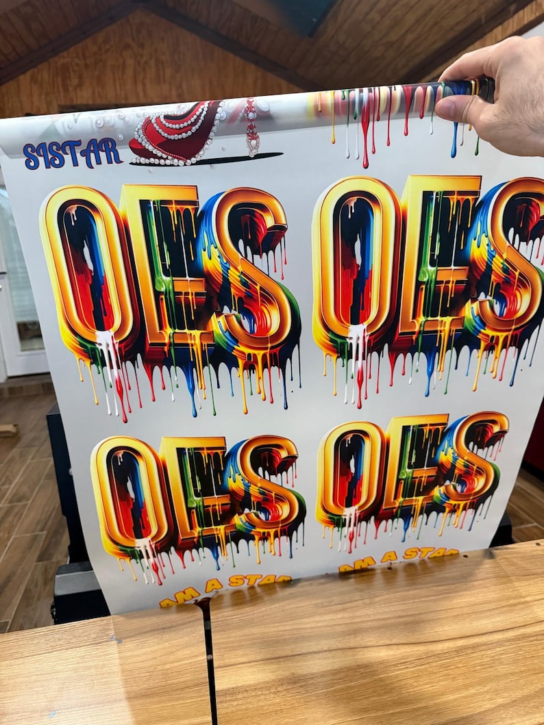 May include: A white background with the words "I AM A STAR" printed in black and the word "OES" printed in large, colorful, dripping letters. The letters are gold with rainbow-colored paint dripping down the sides.