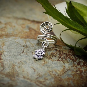 May include: Silver ear cuff with a spiral design and a dangling flower charm. The cuff is made of wire and is designed to fit comfortably on the ear.
