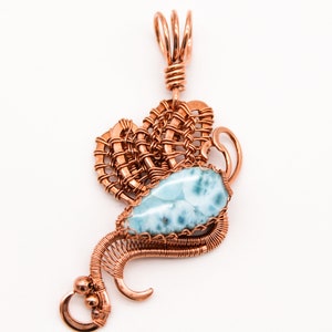 May include: A copper wire wrapped pendant featuring a blue and white gemstone. The pendant has a delicate, intricate design and is perfect for adding a touch of elegance to any outfit.