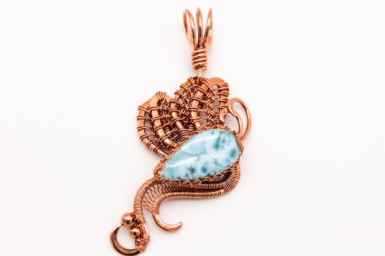 May include: A copper wire wrapped pendant featuring a blue and white gemstone. The pendant has a delicate, intricate design and is perfect for adding a touch of elegance to any outfit.