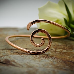May include: A copper bracelet with a spiral design. The bracelet is on a brown, textured surface.