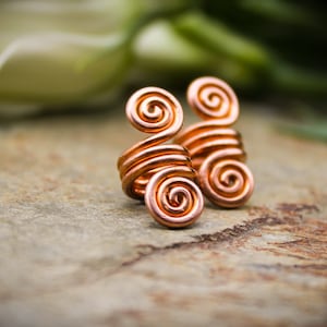 Puede incluir: Dos pendientes de alambre de cobre con un diseño en espiral. Los pendientes están hechos de alambre de cobre fino y están diseñados para envolverse alrededor de la oreja.