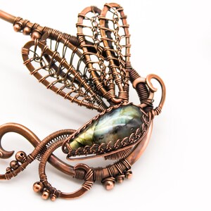 May include: A copper wire dragonfly pendant with a green and blue labradorite gemstone. The dragonfly's wings are made of intricate wirework and the pendant is attached to a copper wire loop.