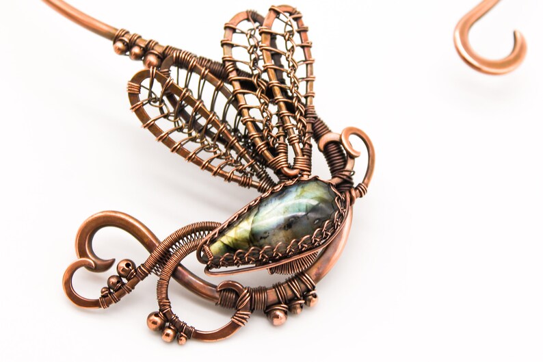 May include: A copper wire dragonfly pendant with a green and blue labradorite gemstone. The dragonfly's wings are made of intricate wirework and the pendant is attached to a copper wire loop.