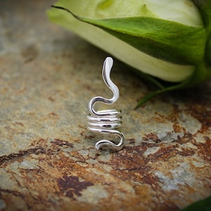 May include: Silver snake ear cuff, coiled and curled, with a smooth, polished finish. The cuff is displayed on a textured, brown surface.
