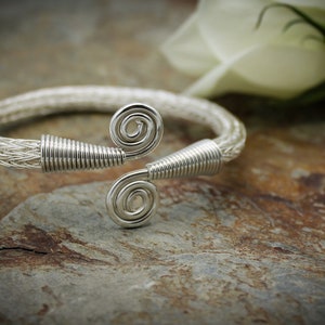 Peut inclure: Un bracelet en fil d'argent avec deux motifs en spirale. Le bracelet est fait de fil fin et a un design délicat et complexe.