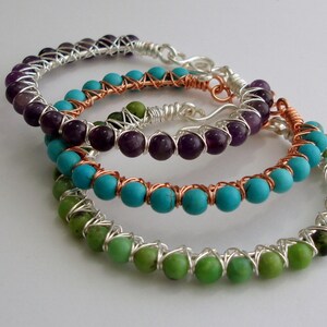 May include: Three wire-wrapped bracelets with different colored gemstones. The top bracelet has amethyst beads, the middle bracelet has turquoise beads, and the bottom bracelet has green beads.
