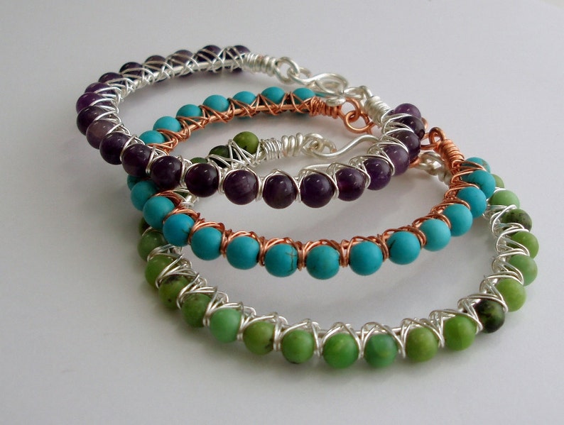 May include: Three wire-wrapped bracelets with different colored gemstones. The top bracelet has amethyst beads, the middle bracelet has turquoise beads, and the bottom bracelet has green beads.