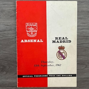Może przedstawiać: Czerwono-biały program meczu piłkarskiego pomiędzy Arsenalem a Realem Madryt. Program zawiera herby drużyn i datę "Czwartek, 13 września 1962". Na dole nadrukowany jest tekst "OFFICIAL PROGRAMME PRICE ONE SHILLING".