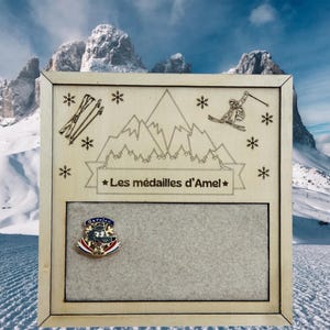 Peut inclure: Une plaque en bois avec une scène de montagne et le texte "Les médailles d'Amel" gravé dessus. La plaque a une petite épingle dorée avec un motif de loup attachée.