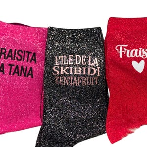 May include: Three pairs of glitter socks in pink, black, and red. The pink sock has the text "Fraisita La Tana", the black sock has "L'ILE DE LA SKIBIDI TENTAFRUIT", and the red sock has "Fraisio" with a white heart.