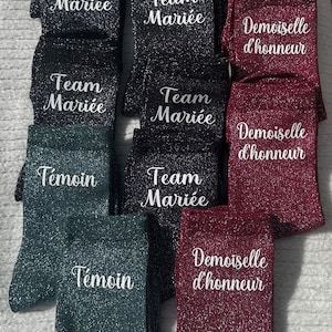 Op de afbeelding: Een set glinsterende sokken met verschillende geprinte zinnen. De sokken zijn in zwart, bordeauxrood en teal. De zinnen op de sokken zijn "Team Mariée", "Demoiselle d'honneur" en "Témoin".