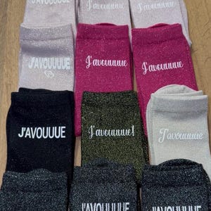 Peut inclure: Une collection de chaussettes scintillantes de différentes couleurs, dont argent, rose, noir et vert olive. Chaque chaussette porte l'inscription "J'AVOUUUUE" en blanc. Les chaussettes sont disposées de manière ordonnée.