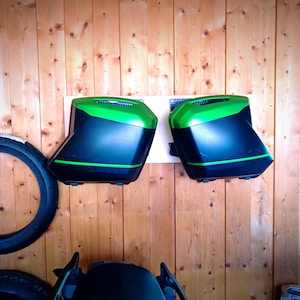 Puede incluir: Dos alforjas de moto negras y verdes montadas en una pared de madera.