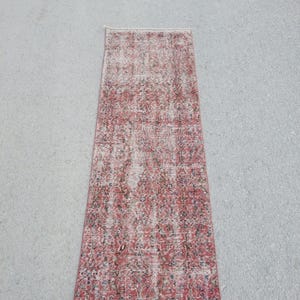 May include: A rectangular rug with a distressed floral pattern in red, white, and dark blue. The rug, placed on a grey surface, has a vintage appearance. The rug's dimensions are not visible.