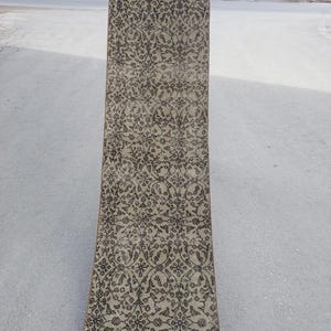 May include: A rectangular, beige rug with an intricate, repeating floral pattern in dark brown. The rug is long and narrow, suitable for a hallway or entryway. The design features stylized flowers and vines.