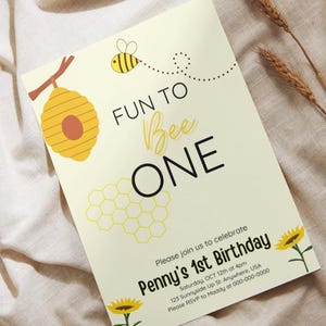 May include: A yellow and black bee with a honeycomb design and the text "Fun to Bee One" on a light yellow background. The text "Please join us to celebrate Penny's 1st Birthday" is at the bottom of the invitation.
