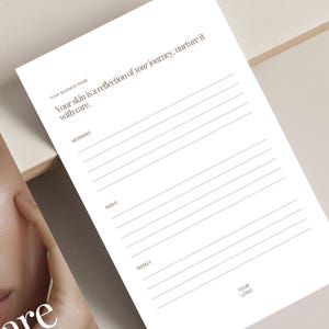 May include: A white skincare journal with lined pages for daily, morning, night, and weekly entries. The journal includes the text "Your skin is a reflection of your journey, nurture it with care." A beauty product is visible in the background.