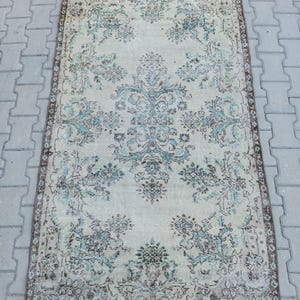 May include: A rectangular vintage rug featuring a cream backdrop and detailed floral patterns in blue, teal, and brown. The rug has a distressed appearance, with a detailed border and a central medallion design.