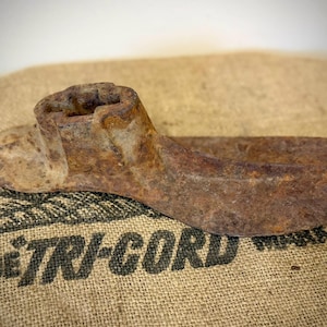 May include: A heavy, cast iron cobbler's shoe last with a deep, uniform brown rust patina covering the entire surface. The object features a raised, hollow heel section and a flat, elongated sole plate, showing signs of age and industrial wear.