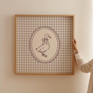This vintage-inspired digital art print features a hand drawn duck with bow illustration and a neutral beige brown gingham background. This square print make the perfect gift for wall decor for a vintage cottage and elegant nursery room for a baby girl or boy, bedroom or even the kids game room.