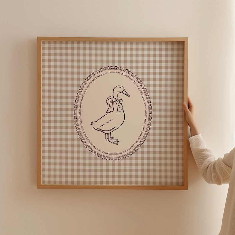 This vintage-inspired digital art print features a hand drawn duck with bow illustration and a neutral beige brown gingham background. This square print make the perfect gift for wall decor for a vintage cottage and elegant nursery room for a baby girl or boy, bedroom or even the kids game room.