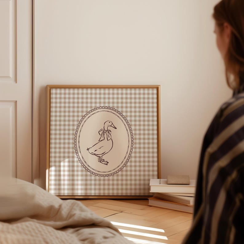 This vintage-inspired digital art print features a hand drawn duck with bow illustration and a neutral beige brown gingham background. This square print make the perfect gift for wall decor for a vintage cottage and elegant nursery room for a baby girl or boy, bedroom or even the kids game room.
