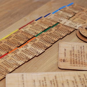 May include: A wooden game with a variety of colored cards, each with a different number and text. The cards are arranged in rows on a wooden surface. There is also a small wooden wheel with a compass-like design.