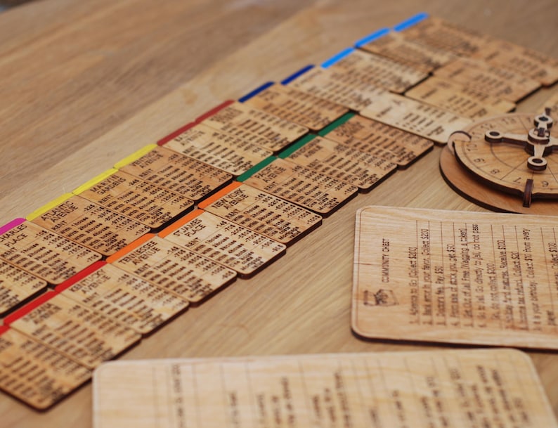 May include: A wooden game with a variety of colored cards, each with a different number and text. The cards are arranged in rows on a wooden surface. There is also a small wooden wheel with a compass-like design.
