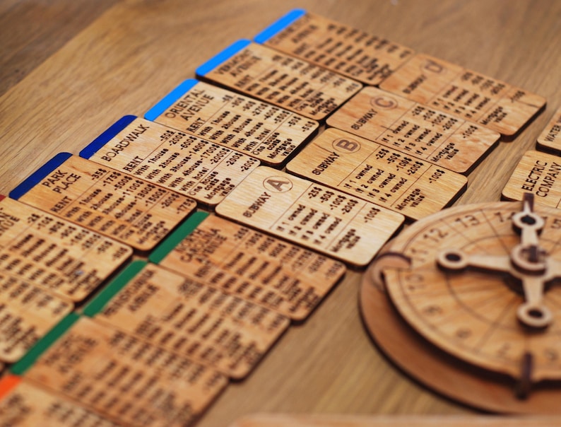 May include: A wooden board game with various property cards, including Park Place, Boardwalk, Oriental Avenue, and a spinning wheel with numbers 1 through 13. The cards have text and numbers printed on them, indicating rent costs and other game details.