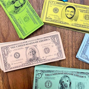 Könnte beinhalten: Ein Stapel gefälschter Geldscheine mit verschiedenen Stückelungen, die verschiedene Personen und einen Hund zeigen. Die Scheine sind mit den Worten "The United States of America" und "One Dollar" bedruckt.