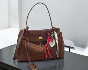 May include: A brown suede handbag with a gold clasp and a key chain with a heart-shaped tag that says "Maybe we'll meet again in another life".