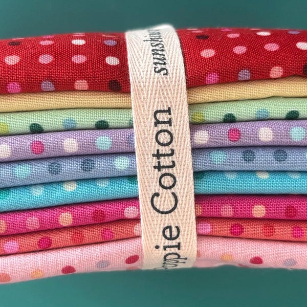 May include: A stack of colorful fabric squares with white polka dots. The fabrics are in shades of red, yellow, green, purple, blue, and pink. A cream-colored ribbon with the text "pie Cotton" wraps around the stack.