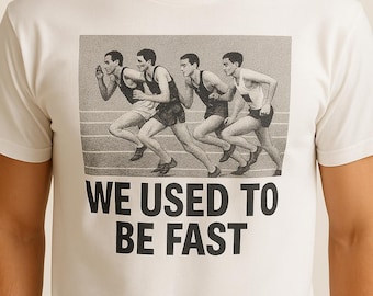 Pode incluir: Camiseta branca com um gráfico em preto e branco de quatro corredores em uma corrida. O texto "WE USED TO BE FAST" é impresso em letras pretas em negrito abaixo do gráfico. A camiseta é feita de um material macio.