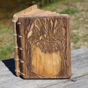 Puede incluir: Un diario de madera hecho a mano con un dise&ntilde;o de &aacute;rbol tallado en la portada. El diario est&aacute; encuadernado con hilo y tiene una est&eacute;tica r&uacute;stica y natural. Las p&aacute;ginas son visibles y la madera tiene un tono marr&oacute;n c&aacute;lido.