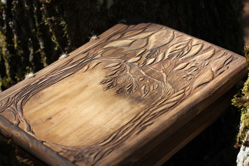 Puede incluir: Un diario de madera con un detallado tallado de &aacute;rbol en la portada. El dise&ntilde;o presenta un &aacute;rbol con hojas y ramas, sobre un fondo marr&oacute;n claro. El diario es rectangular y parece hecho a mano.