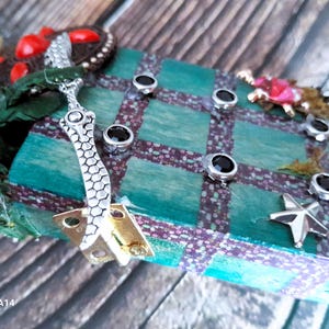 May include: A teal and brown checkered wooden box with a silver decorative piece and black rhinestones. The box has a star-shaped design on the front.